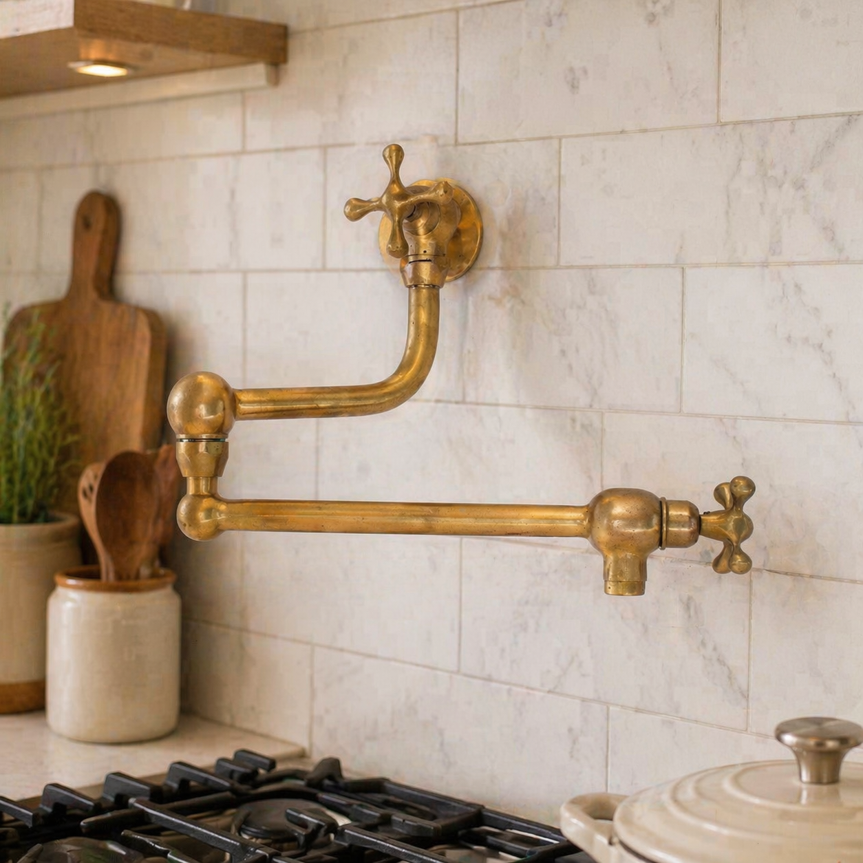 Handmade unlacquered solid brass wall-mounted pot filler faucet with double swing arms and dual shut-off valves installed above a kitchen stove.