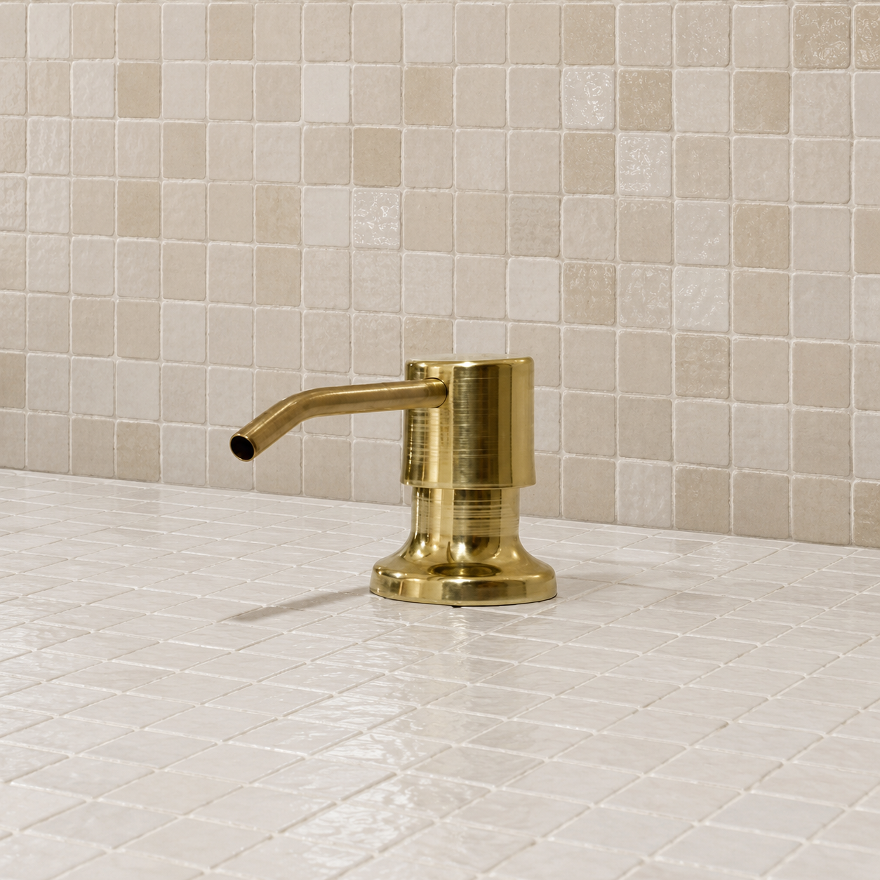Handcrafted solid brass built-in sink soap dispenser installed on a countertop beside a brass kitchen sink.
